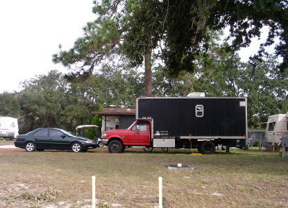 [Green car and red truck with black box converted to an RV.]